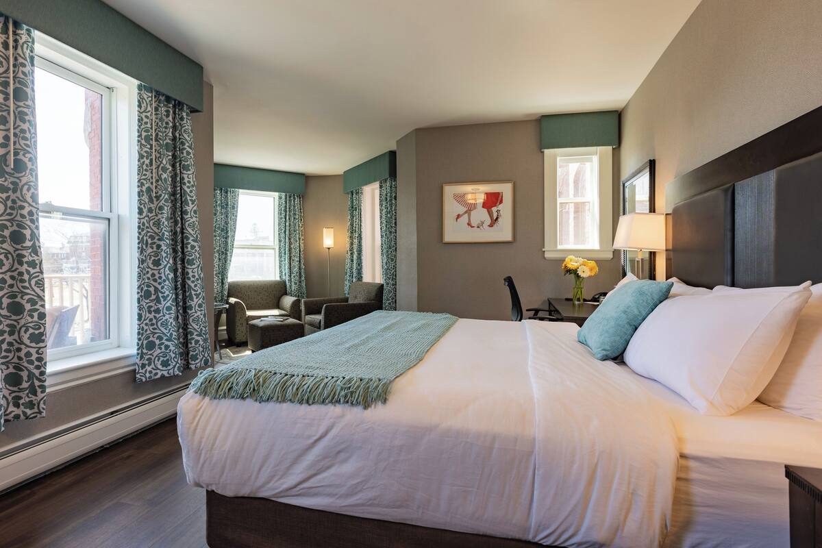 A hotel room with a large bed, a desk, a chair, and a window with curtains.