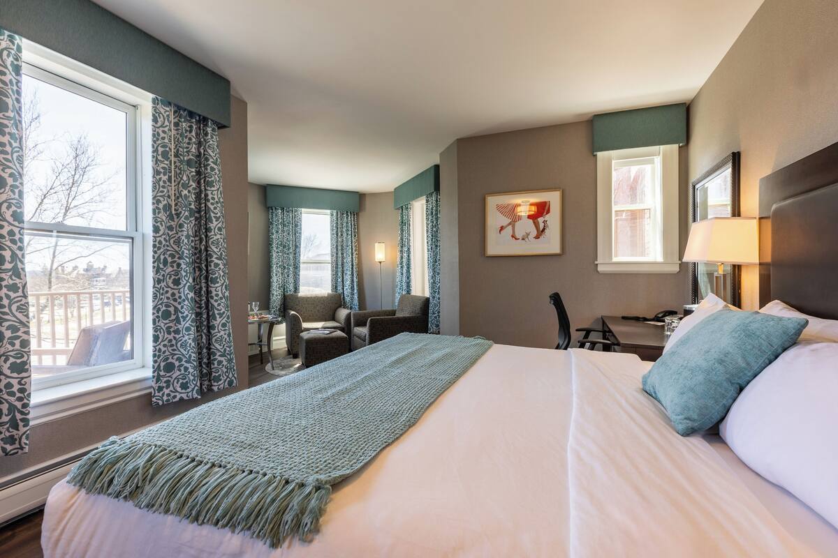 A hotel room with a large bed, a desk, a chair, and a view of the outside.