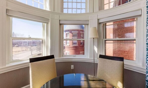 A room with a bay window, a table with chairs, and a lamp.