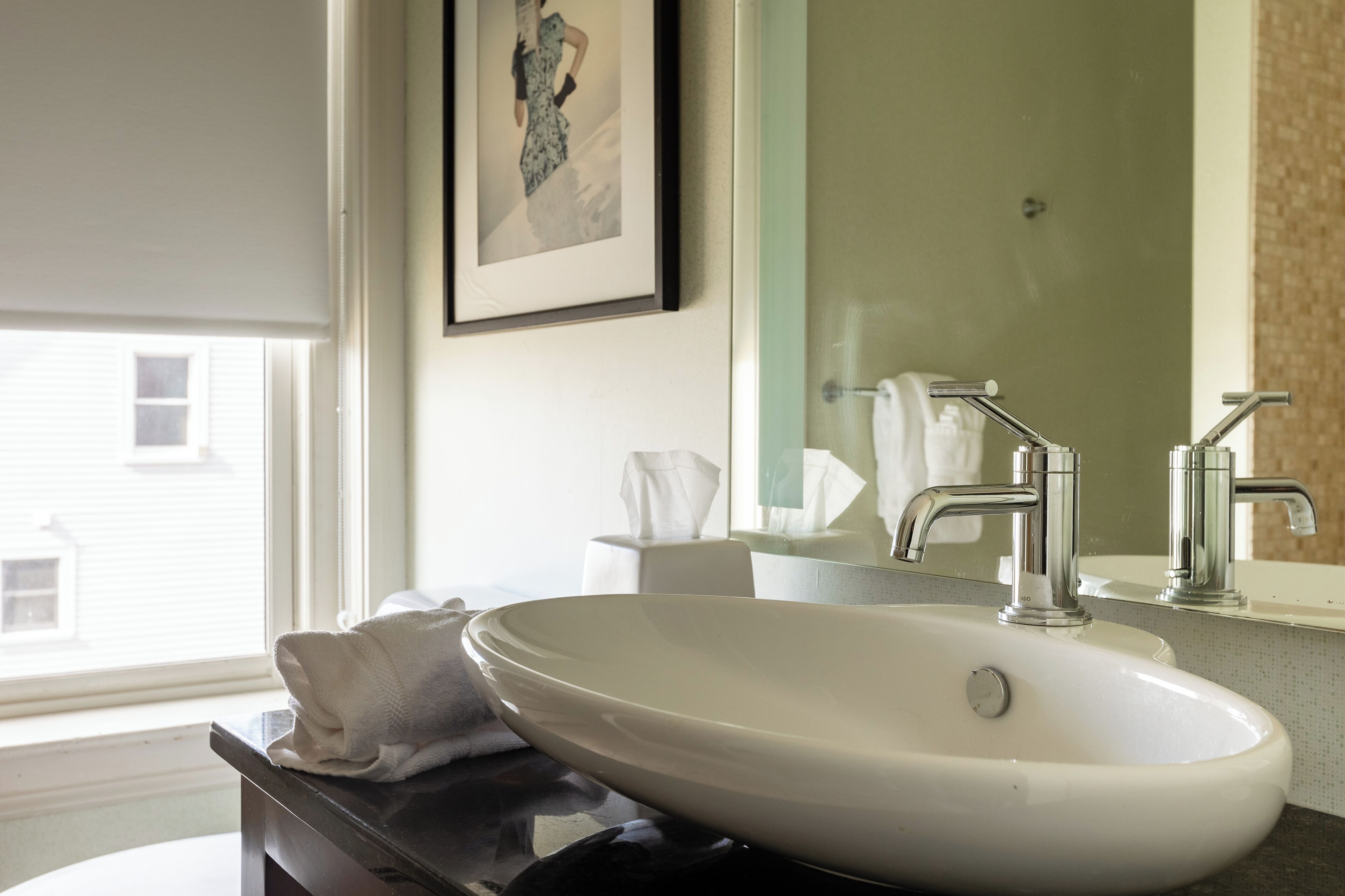 Une salle de bain avec un lavabo blanc, deux robinets, une serviette et un tableau encadré au mur.