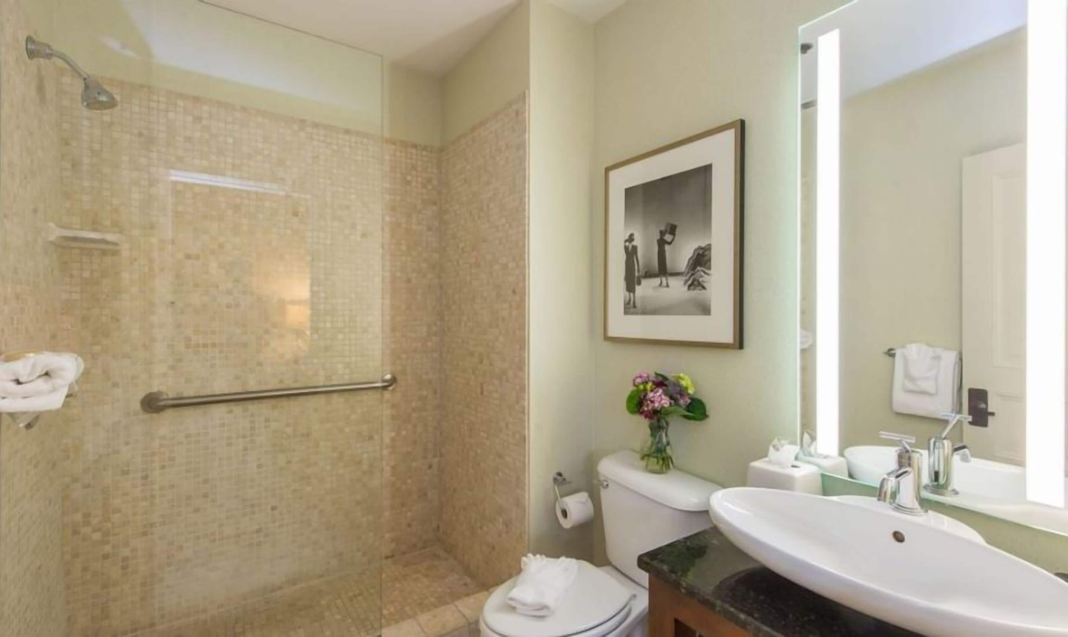 A bathroom with a shower, toilet, sink, and a framed picture on the wall.