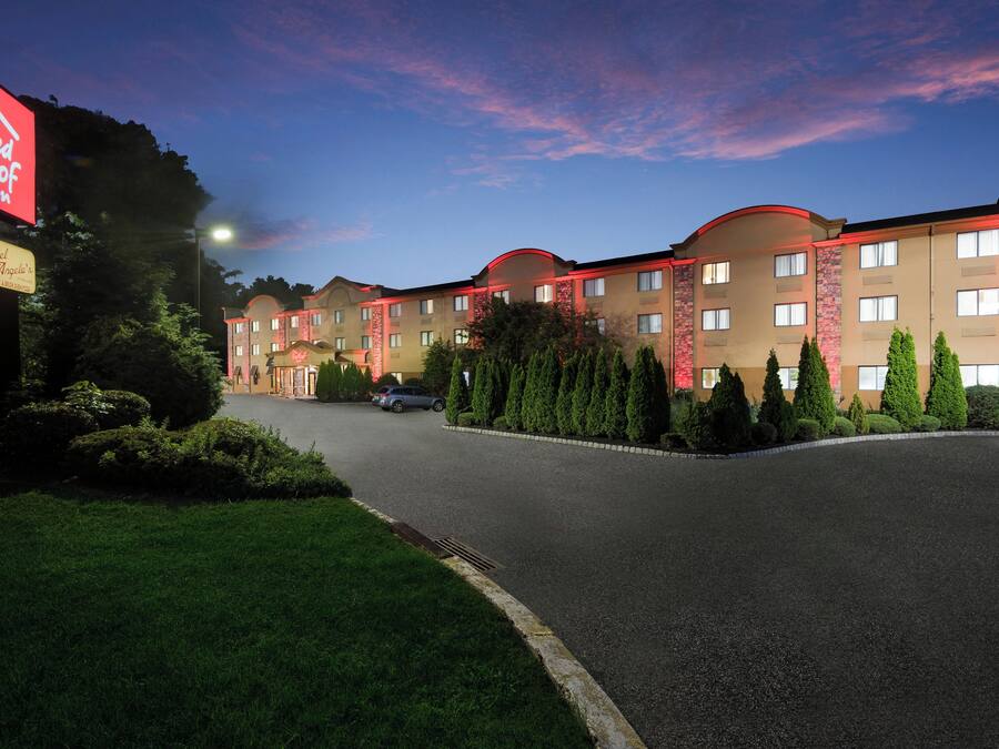A hotel with a parking lot, a red neon sign, and a well-maintained lawn.