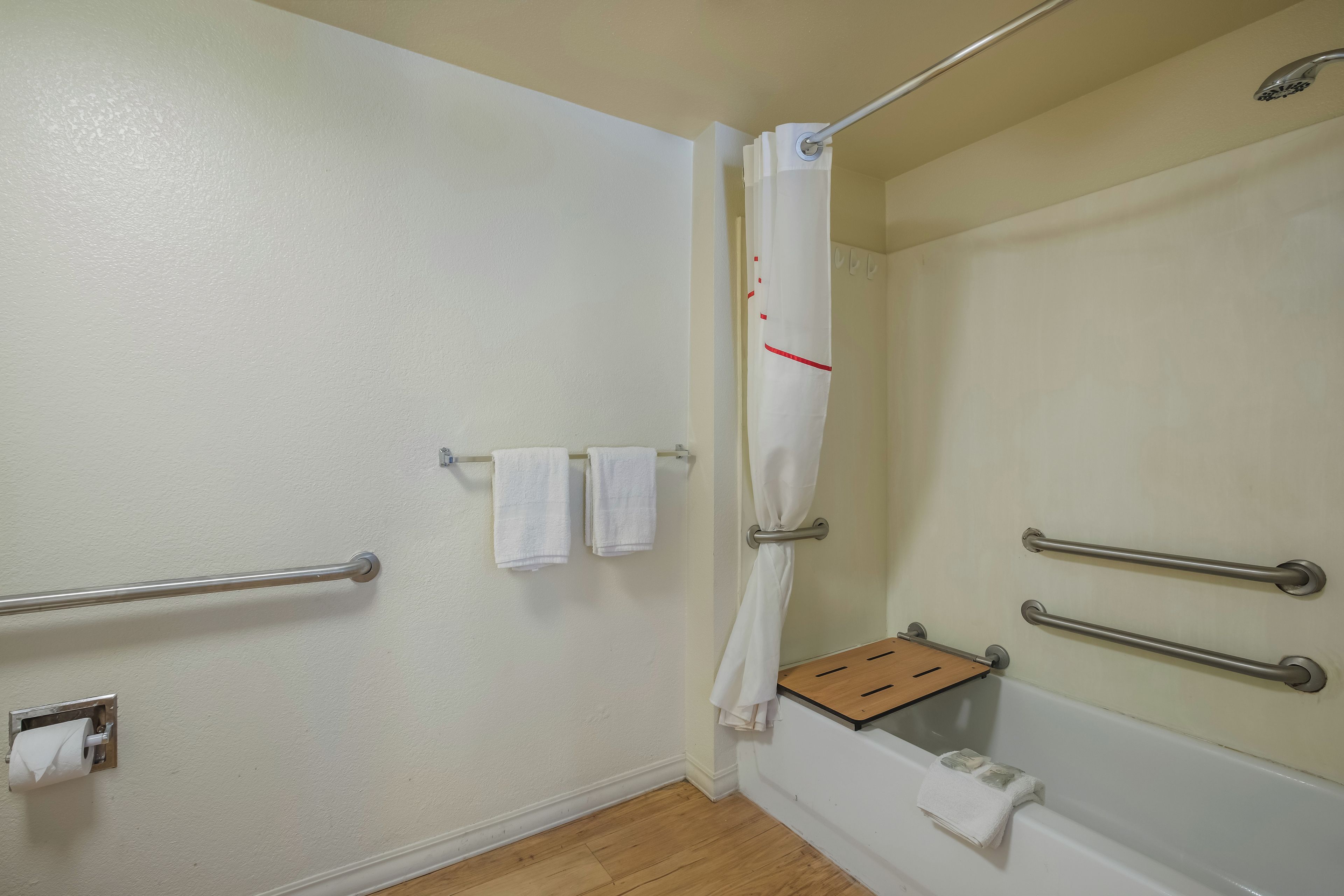 A bathroom with a shower, handrails, a towel rack, and a toilet paper holder.