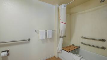 A bathroom with a shower, handrails, a towel rack, and a toilet paper holder.
