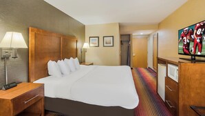 A hotel room with a large bed, bedside lamps, a flat-screen TV, a microwave, and a door leading to a bathroom.