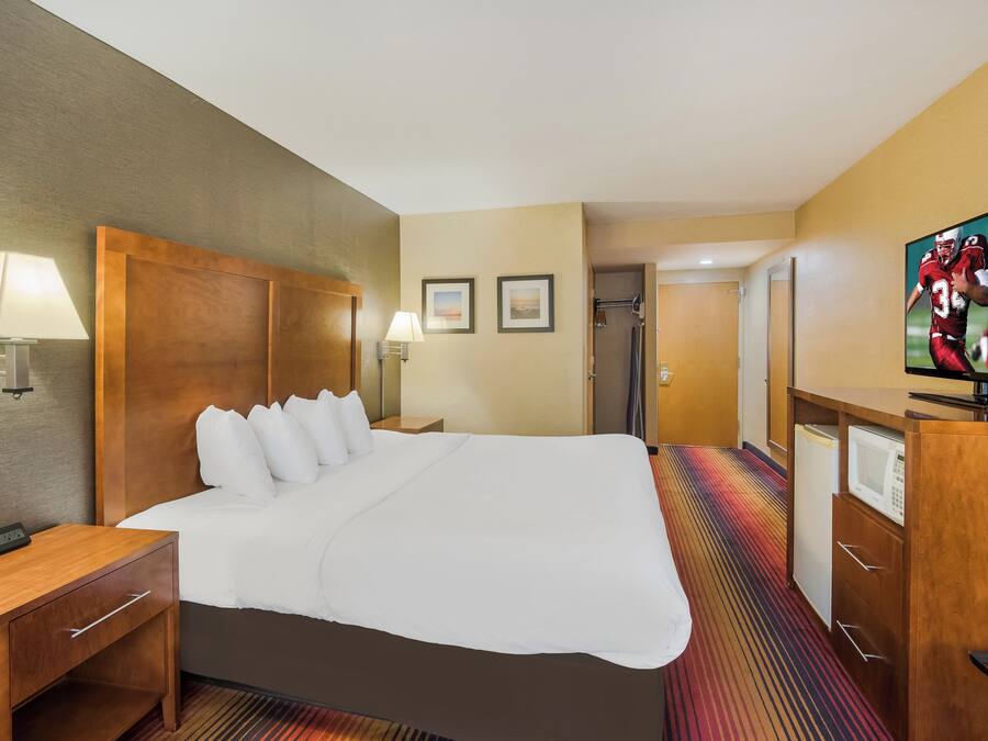 A hotel room with a large bed, bedside lamps, a flat-screen TV, a microwave, and a door leading to a bathroom.