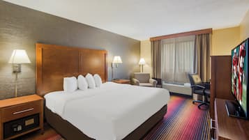 A hotel room with a large bed, two bedside tables with lamps, a desk with a chair, a television, and a window with curtains.