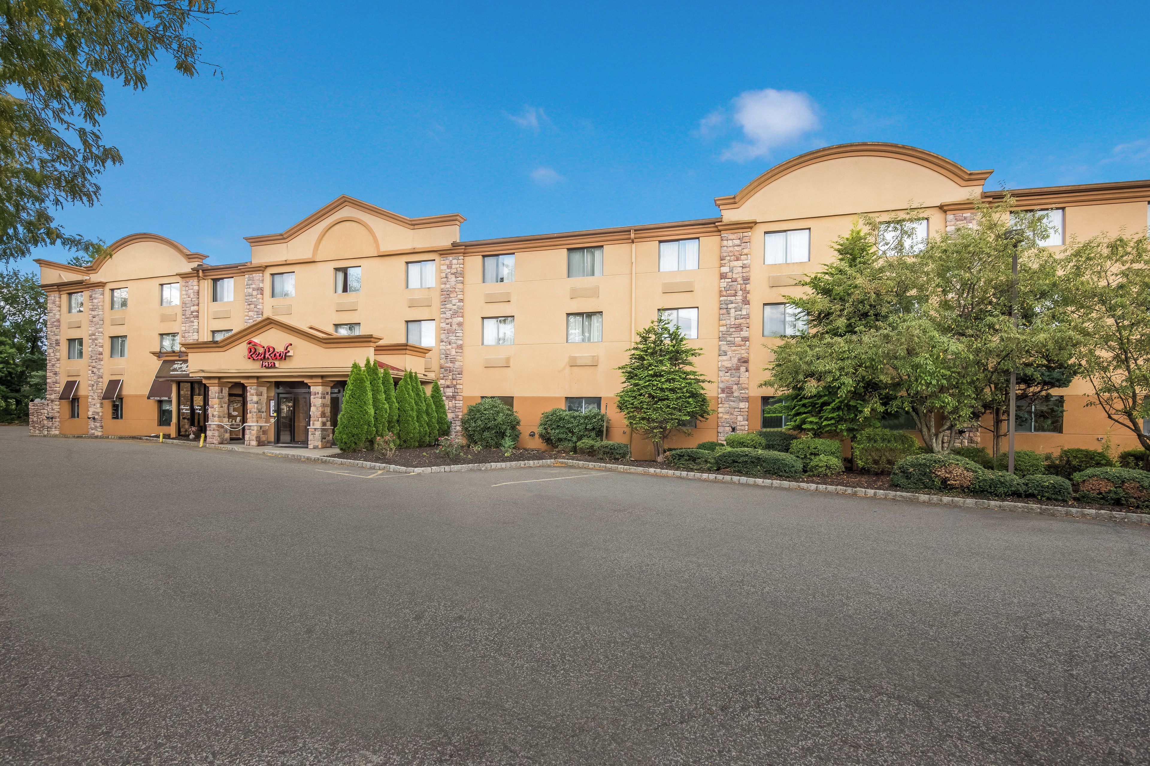 A Red Roof Inn with a two-story structure, a parking lot in front, and a landscaped area with trees.