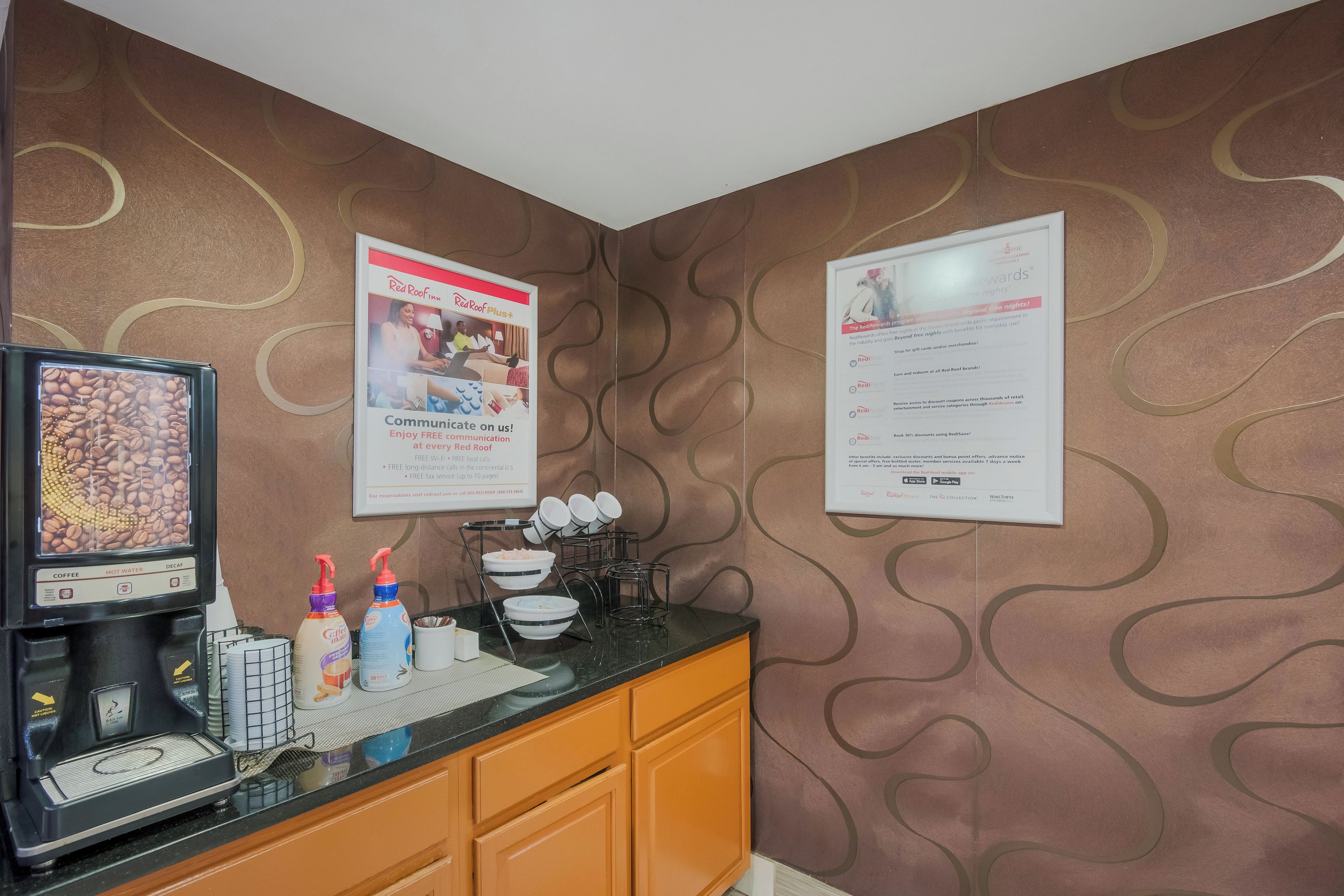 A hotel room with a coffee machine, a Red Roof Plus sign, and a Red Roof Rewards sign.