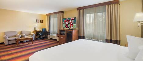 A hotel room with a large bed, a desk with a computer, a chair, a TV, and a window with curtains.