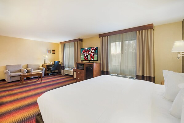 A hotel room with a large bed, a desk with a computer, a chair, a TV, and a window with curtains.