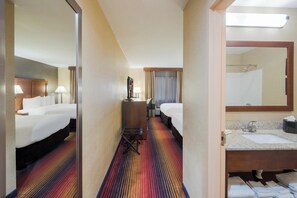 A hotel room with a large bed, a desk with a chair, a bathroom with a sink and mirror, and a colorful striped carpet. - Red Roof Inn Fairfield (Fairfield)
