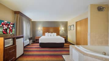 A hotel room with a large bed, a desk, a flat-screen TV, a microwave, a bathroom with a bathtub, and a shower.