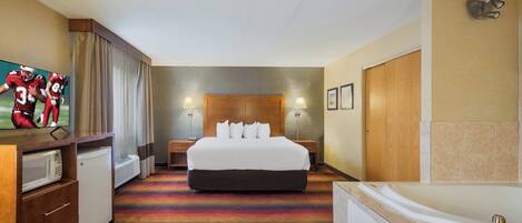 A hotel room with a large bed, a desk, a flat-screen TV, a microwave, a bathroom with a bathtub, and a shower.