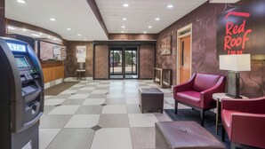 Vestíbulo de Red Roof Inn con piso a cuadros, un mostrador de recepción, un letrero de Red Roof Inn, un sillón de cuero rojo y un cajero automático.
