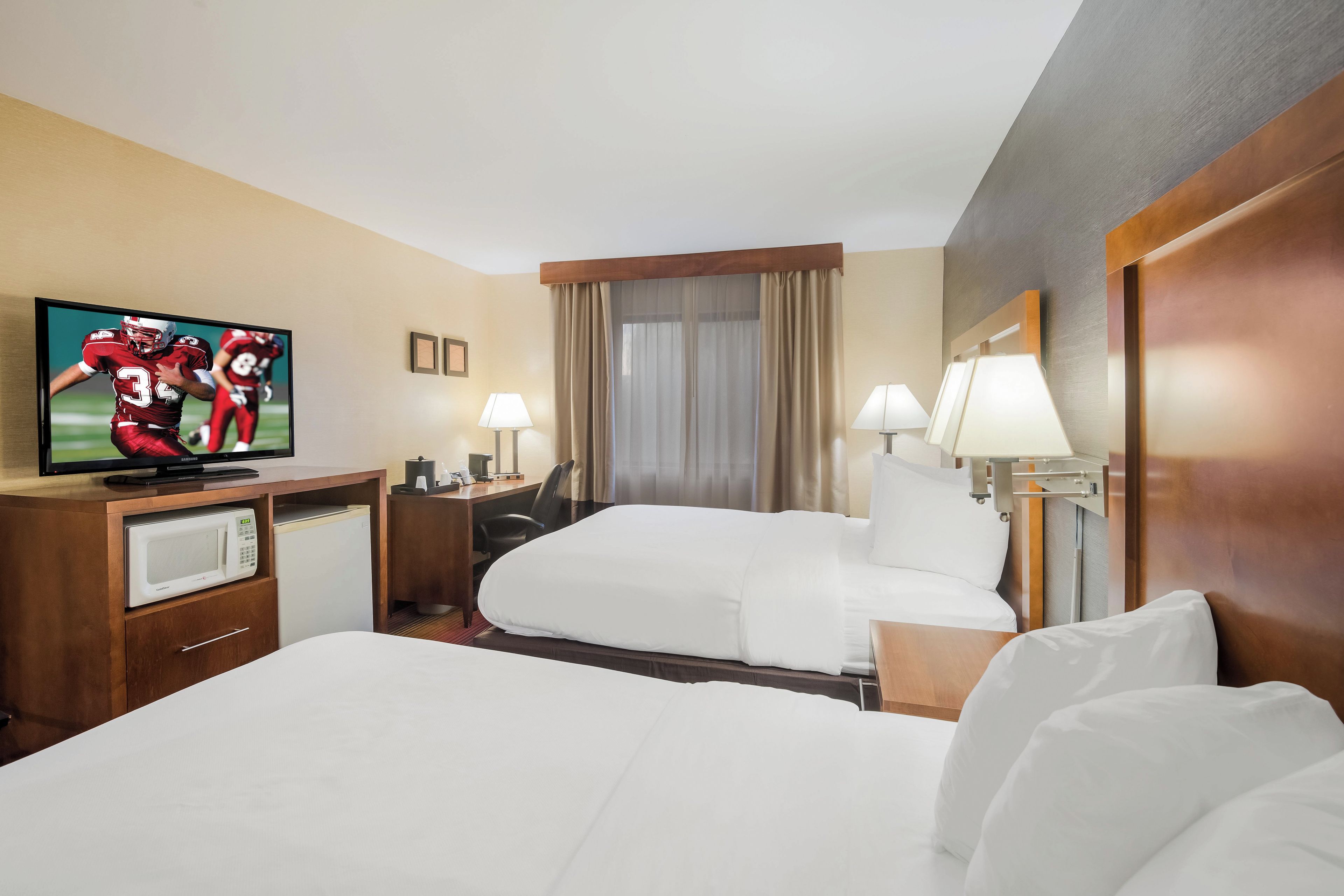 Ein Hotelzimmer mit einem Bett, einem Schreibtisch mit Fernseher, einer Mikrowelle und zwei Lampen.