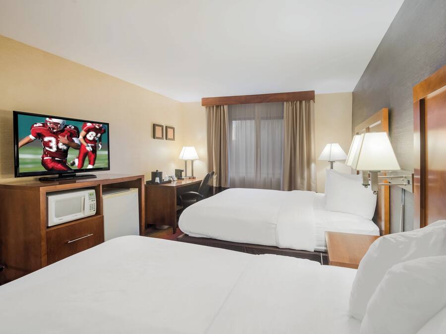 Una habitación de hotel con una cama, un escritorio con televisor, un microondas y dos lámparas.