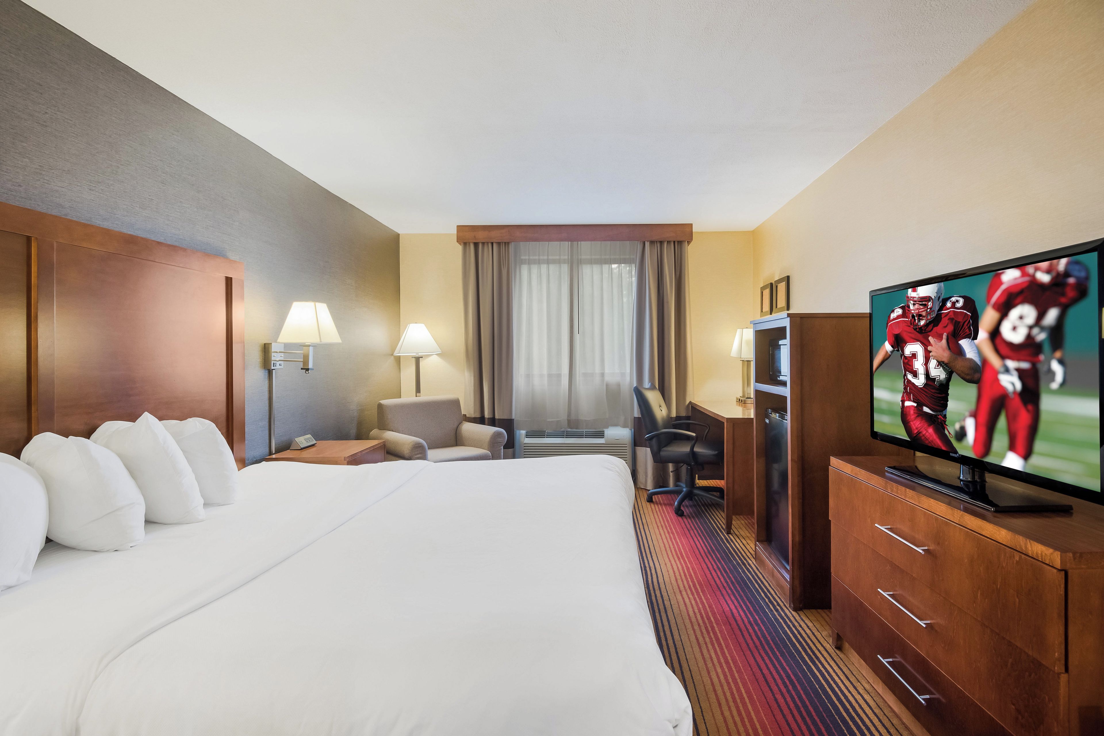Habitación de hotel con una cama grande, un escritorio con silla, televisor y ventana con cortinas.