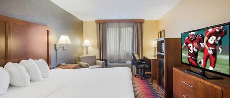 Habitación de hotel con una cama grande, un escritorio con silla, televisor y ventana con cortinas.