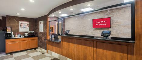 A hotel reception area with a check-in counter, a coffee machine, and a sign indicating free Wi-Fi in all rooms.