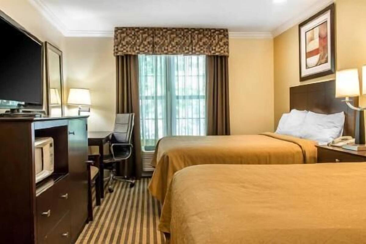 A hotel room with a bed, a desk, a chair, a television, and a window with curtains.