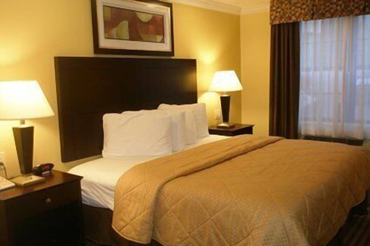 A hotel room with a large bed, two bedside tables, a headboard, a painting on the wall, and a window with curtains.