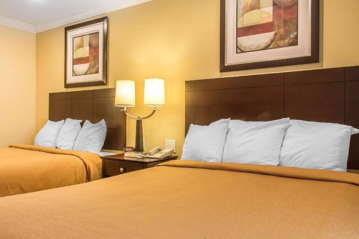 A hotel room with two beds, a nightstand with a phone, and wall-mounted lamps.