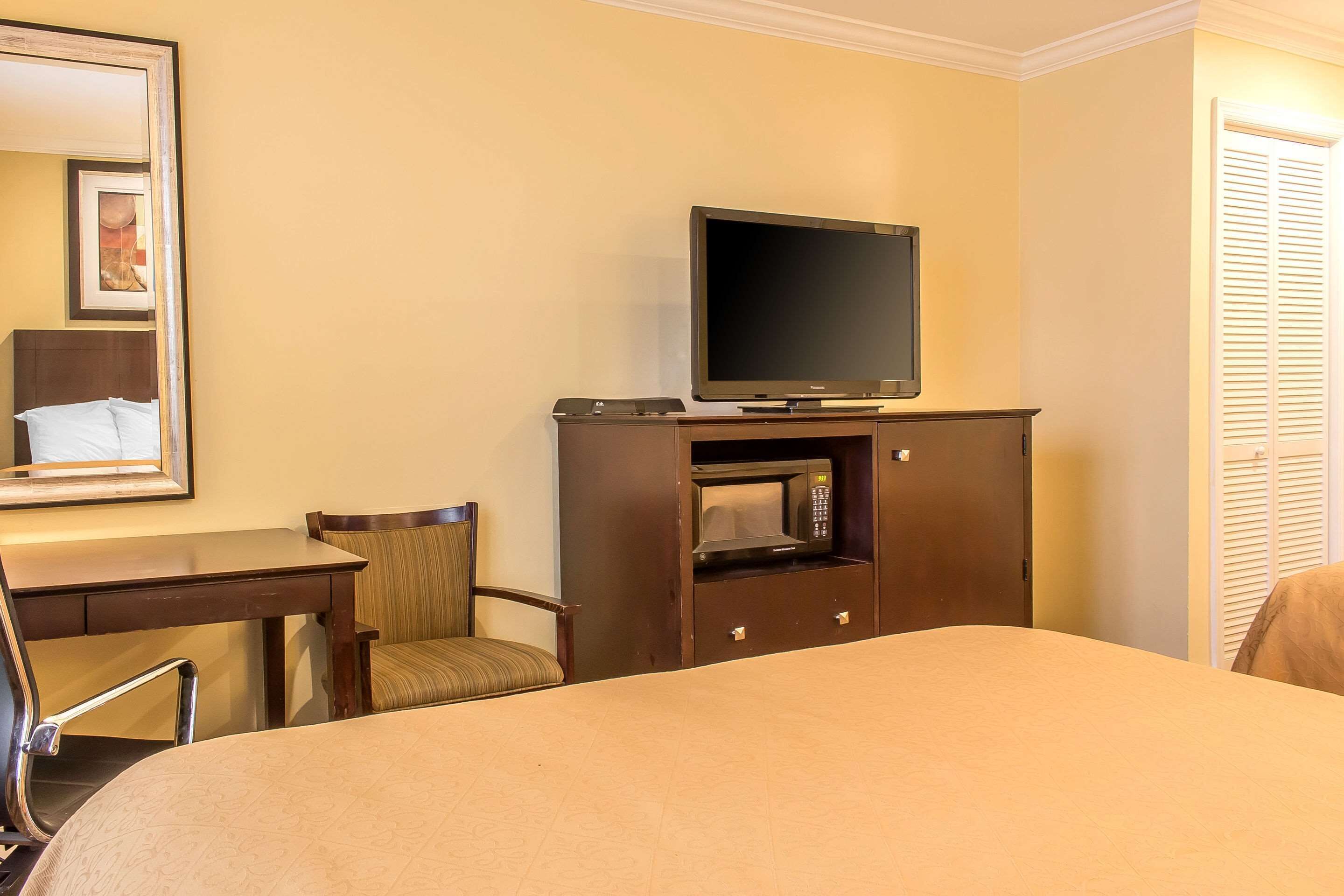 A hotel room with a bed, a TV on a wooden stand, a desk with a chair, and a microwave.