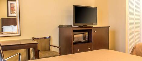 A hotel room with a bed, a TV on a wooden stand, a desk with a chair, and a microwave.