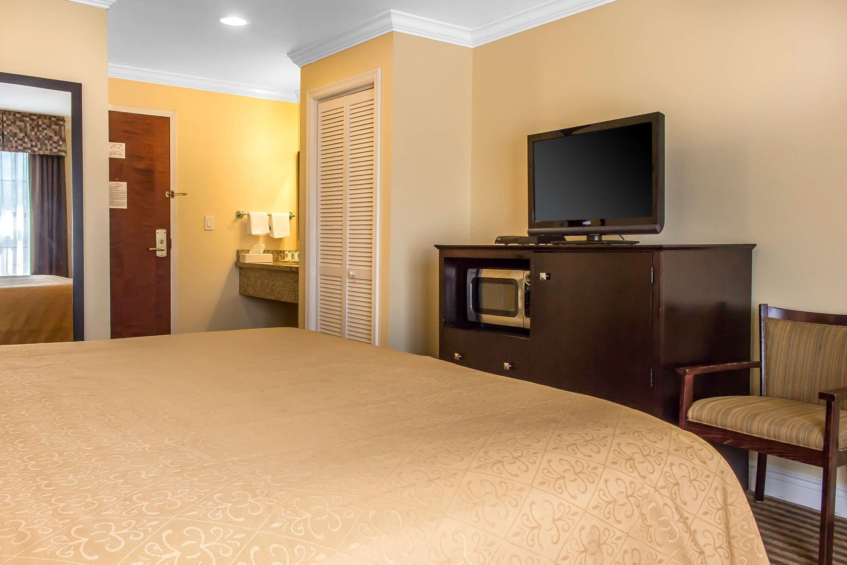 A hotel room with a large bed, a television on a wooden cabinet, a chair, and a door with a towel hanging on it.