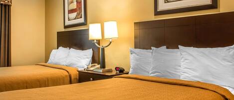 Quarto de hotel com duas camas, cada uma com colcha marrom, mesa de cabeceira com luminária e obras de arte emolduradas nas paredes.