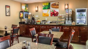 A hotel dining area with granite tables, wooden chairs, a coffee machine, a fruit bowl, and a refrigerator with beverages. - Quality Inn near Mountain Creek (Vernon)