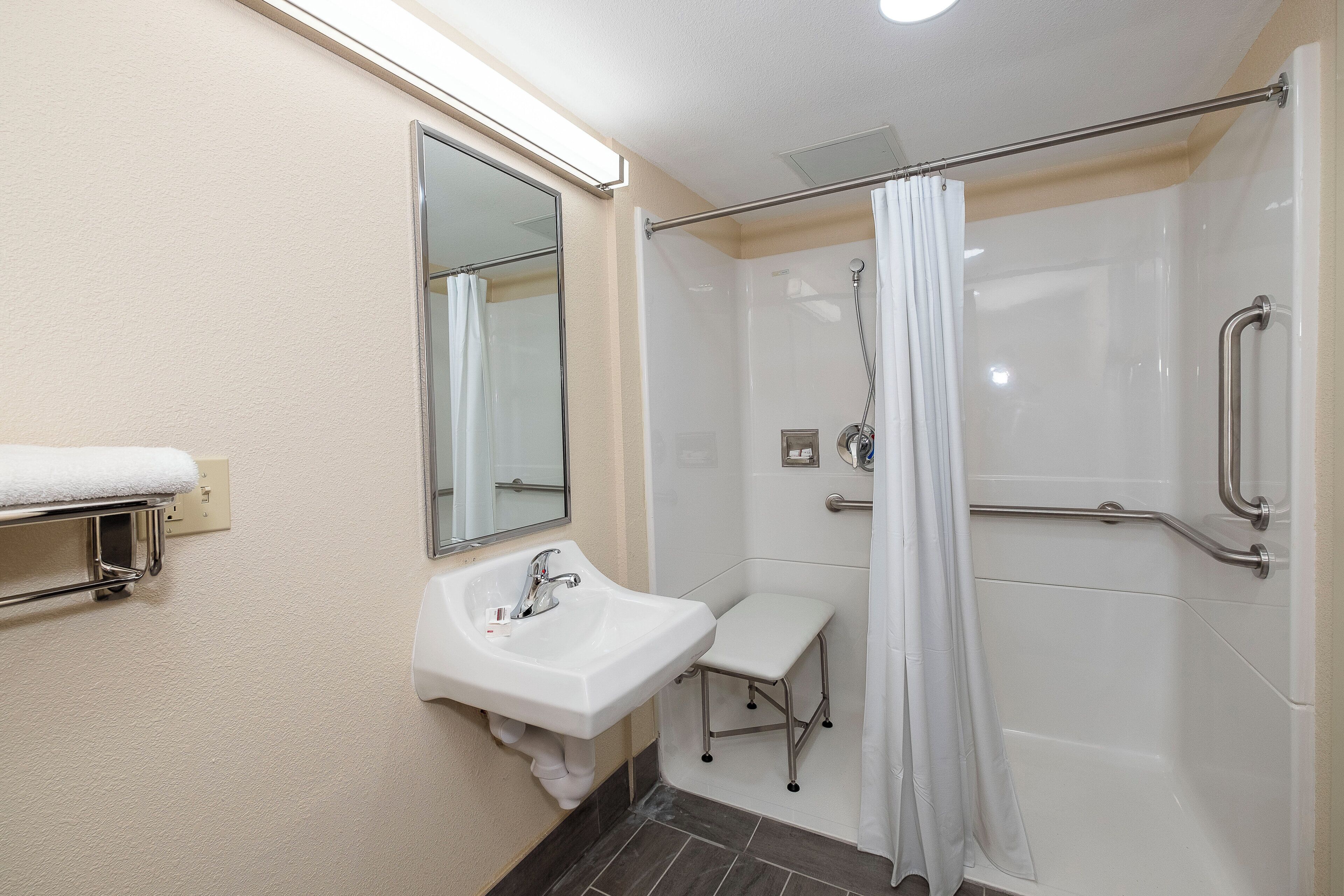 A bathroom with a white sink, mirror, and shower area with grab bars.