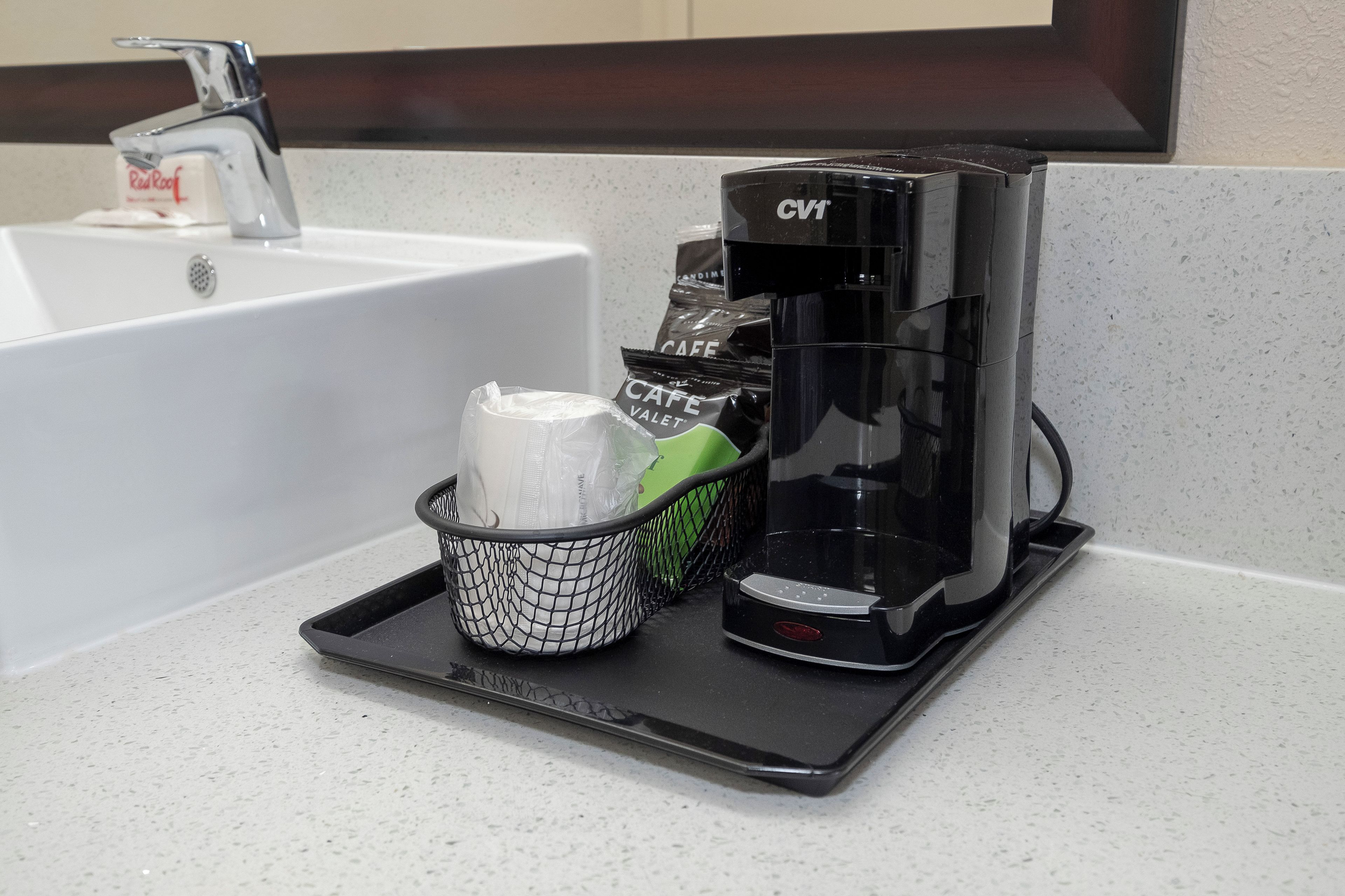 A coffee maker on a countertop with a tray, a basket with a white object, and a bag of coffee creamer.
