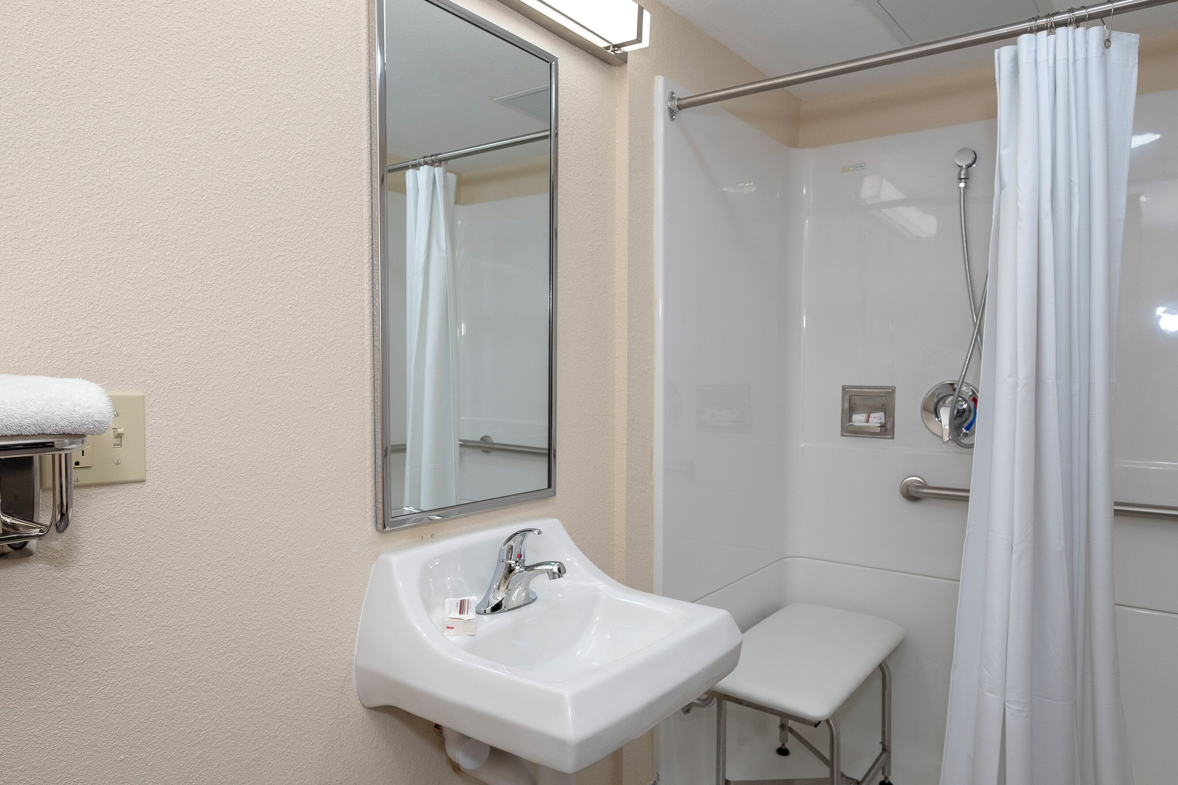 Un baño con un lavabo blanco, un espejo, una ducha con puerta de cristal y un perchero para toallas.