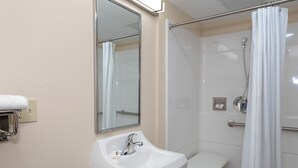 A bathroom with a white sink, a mirror, a shower with a glass door, and a towel rack. - Red Roof Inn Freehold (Freehold)
