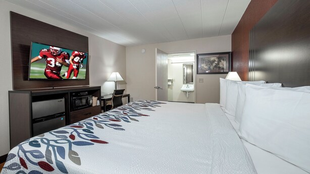 A hotel room with a large bed, a flat-screen TV mounted on the wall, a desk with a lamp, a microwave, and a refrigerator. - Red Roof Inn Freehold (Freehold)