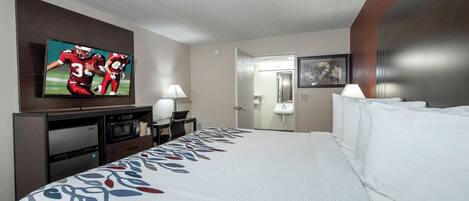 Habitación de hotel con una cama grande, un televisor de pantalla plana en la pared, un escritorio con lámpara, microondas y refrigerador.