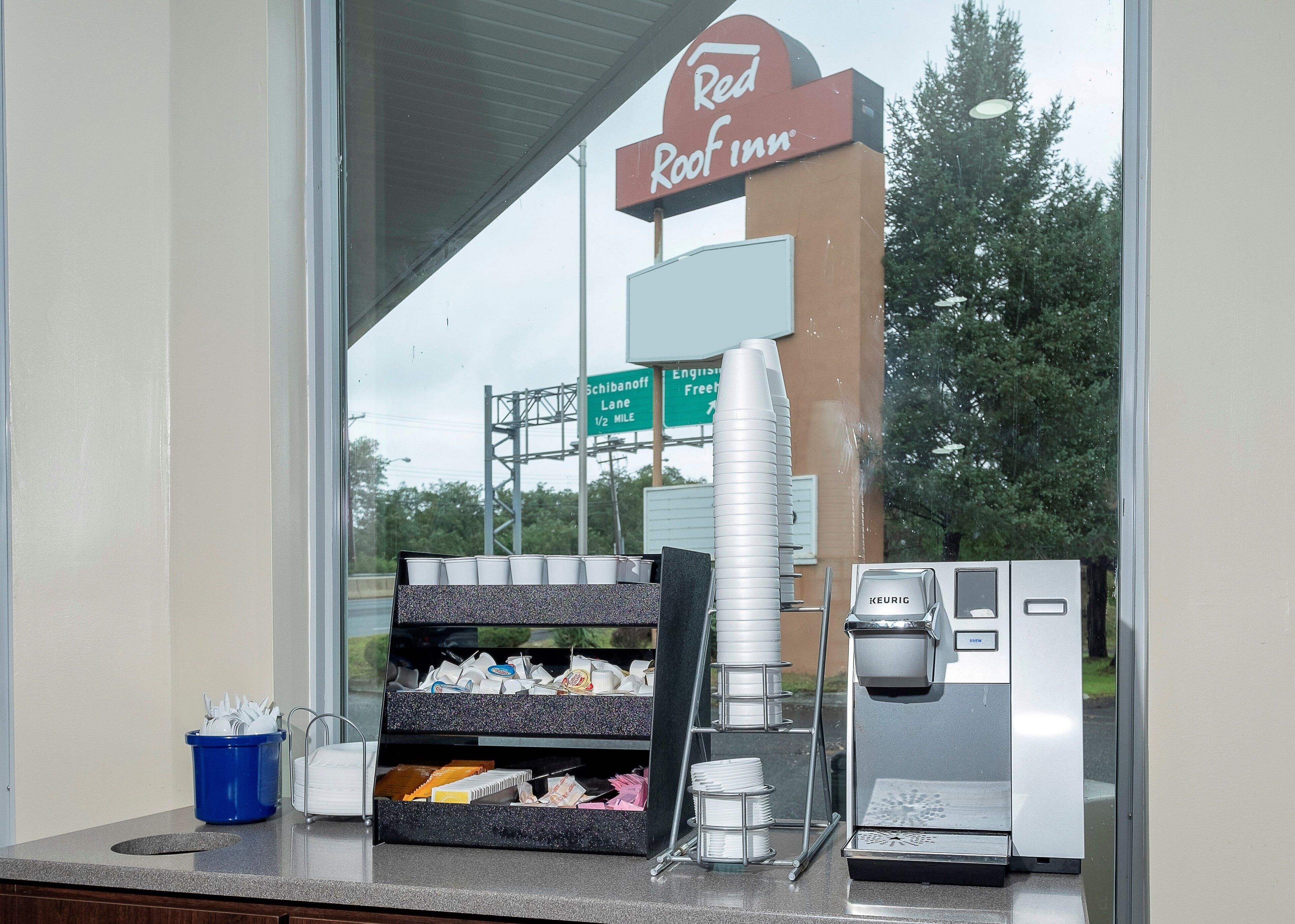 Ein Kaffee-Bereich mit einer Keurig-Maschine, Einwegbechern und einem blauen Mülleimer im Red Roof Inn.