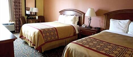 A hotel room with two beds, a desk, a chair, a lamp, and a clock on the wall.