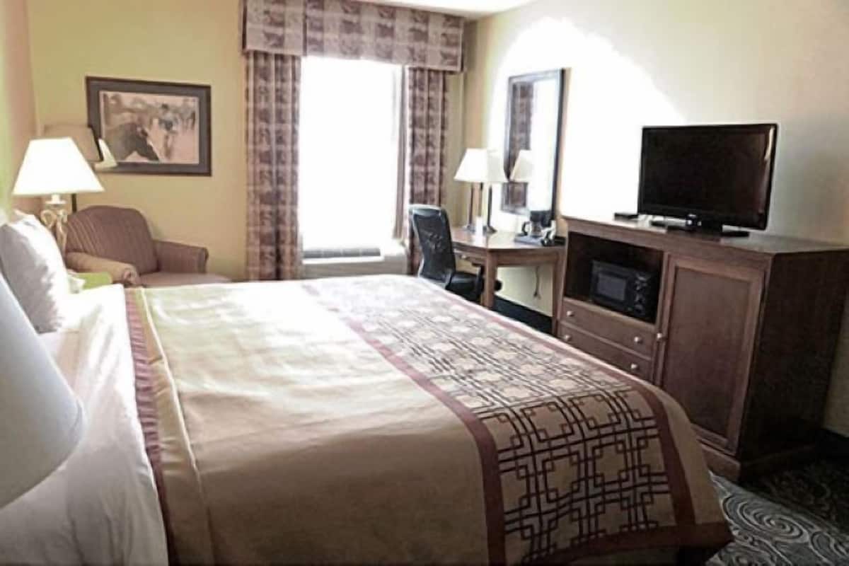 Ein Hotelzimmer mit Bett, Schreibtisch, Sessel, Fernseher und einem Fenster mit Vorhängen.