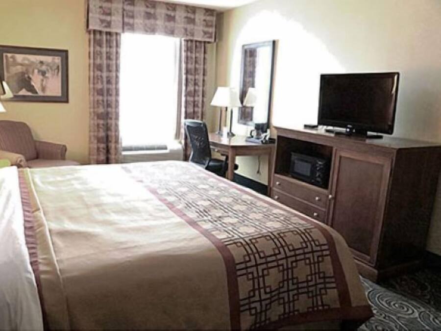 Una habitación de hotel con cama, escritorio, silla, televisión y ventana con cortinas.
