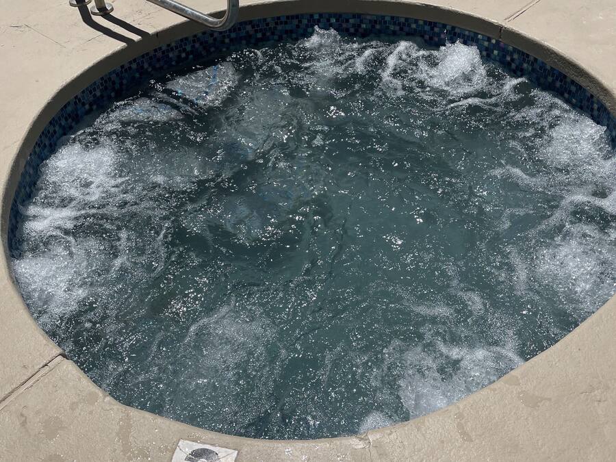 A hot tub with a metal ladder, surrounded by a tiled pool area.