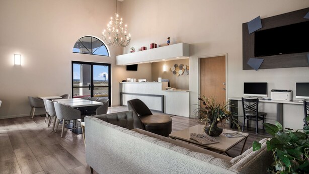 Een moderne woonkamer met een bank, salontafel en eethoek. Er is een keuken met een aanrecht en een grote televisie aan de muur bevestigd.