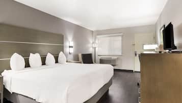 A hotel room with a large bed, bedside tables, a desk, a chair, a flat-screen TV, and a window with blinds.