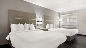 Een hotelkamer met twee bedden, een grote spiegel, een nachtkastje met lamp en een raam met luxaflex.