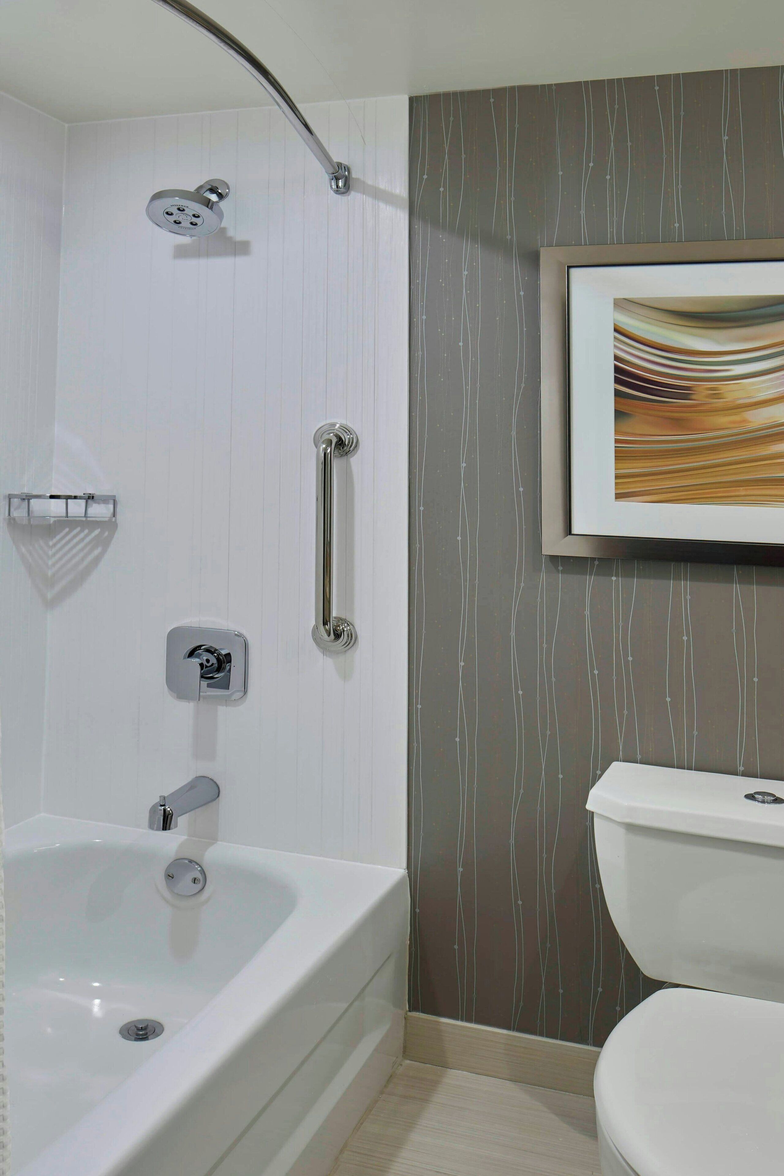 A bathroom with a bathtub, toilet, and a framed picture on the wall.