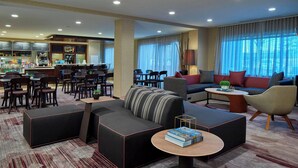 A modern hotel lobby with a seating area, a bar, and a dining space. - Courtyard by Marriott Albany Thruway (Albany)