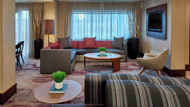 A modern living room with a sectional sofa, a round coffee table, and a TV mounted on the wall. - Courtyard by Marriott Albany Thruway (Albany)