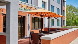 An outdoor seating area with tables and chairs, a large umbrella, and a building with a sign that reads "THE BISTRO". - Courtyard by Marriott Albany Thruway (Albany)